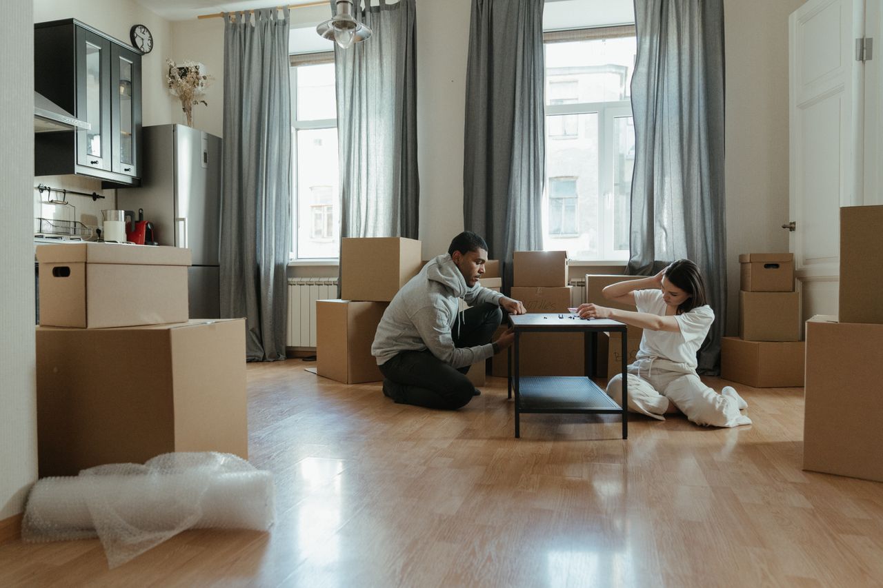 Young couple putting together furniture in their new apartment, with cardboard boxes all around.